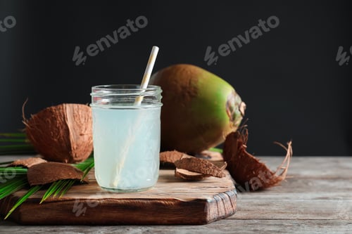 Preview: Beautiful composition with glass jar of coconut water on table against dark background