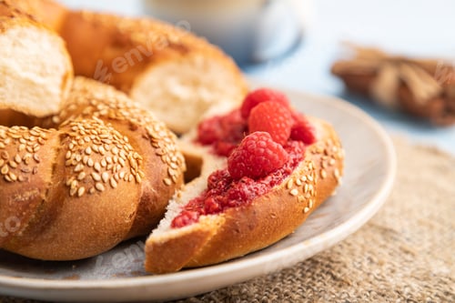 Preview: Homemade sweet bun with raspberry jam and cup of coffee on a blue wooden