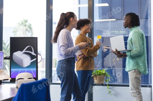 Preview: A diverse group of young colleagues discussing in office, holding papers and laptop