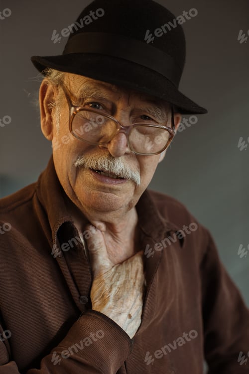 Preview: The old generation. Portrait of a senior man in glasses and a hat on a gray background.