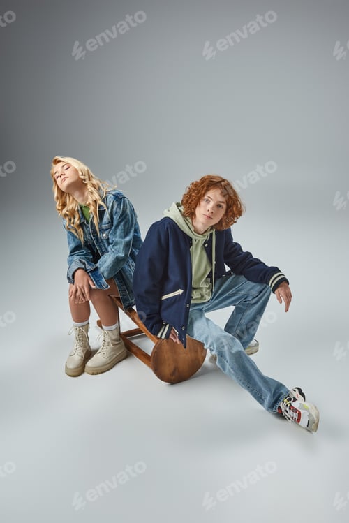 Preview: redhead teen guy in trendy casual wear looking at camera near blonde girlfriend sitting on grey