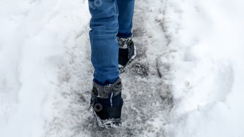 Preview: Closeup of child's feet in snow boots walking on road covered with snow after storm