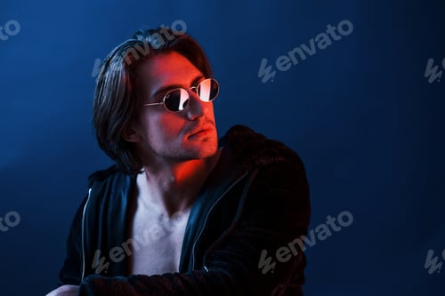 Preview: Beautiful man in glasses and black clothes is in the studio with blue neon lighting