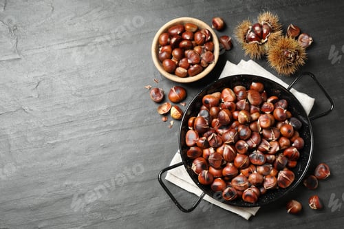 Preview: Delicious roasted edible chestnuts on black slate table, flat lay. Space for text
