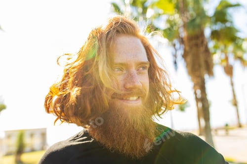Preview: handsome redhaireb man with long beard wear black sporty suit and warming up in sunny beach
