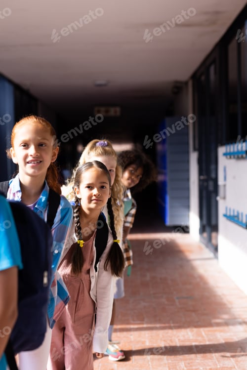 Preview: Vertical of diverse group of smiling elementary schoolgirls queuing in school corridor, copy space
