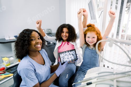 Preview: Smiling happy children, two multiracial girls, visiting dentist, sitting in dental chair