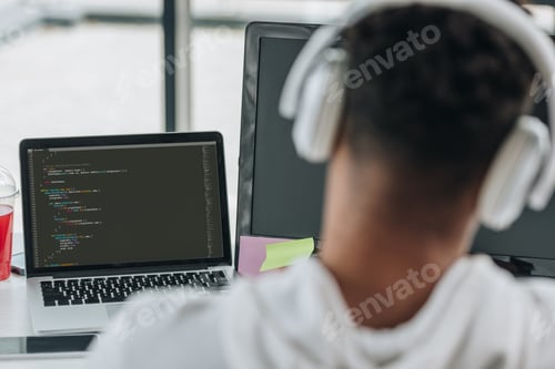 Preview: back view of african american programmer in headphones working on laptop in office