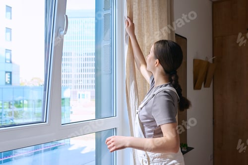 Preview: A young female opens or closes curtains, at home on window