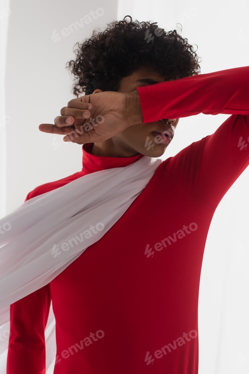 Preview: african american man in red turtleneck obscuring face with arm while posing in white chiffon cloth