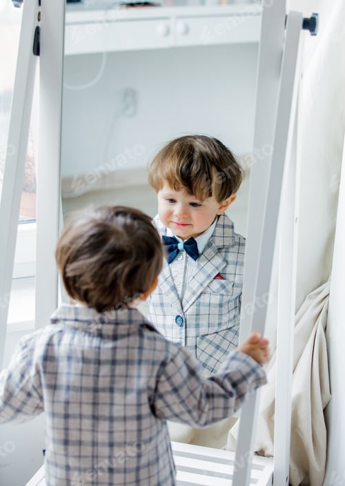Preview: a little boy dressed in a suit looks at himself in the mirror