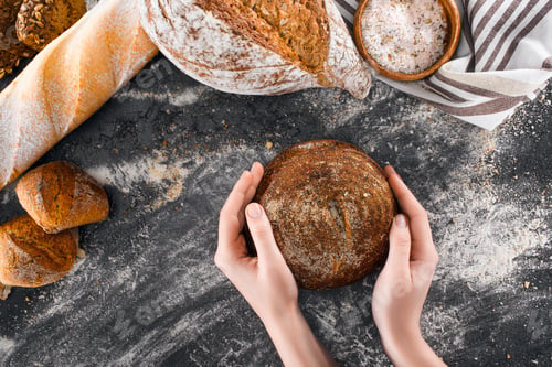 Preview: cropped shot of human hands holding loaf of healthy homemade bread