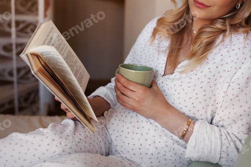 Preview: Close up Pregnant woman sitting at home in bed, reading book and drinking tea or water from cup