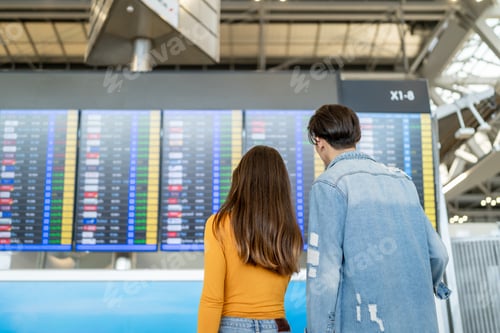 Preview: Rear view of passengers checking flight information on timetable in airport.