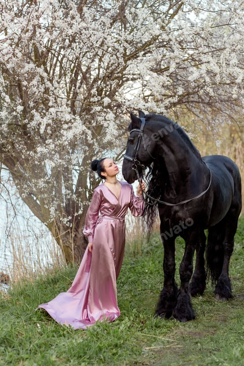 Preview: a girl with dark hair and a beautiful black horse against the background of a flowering tree