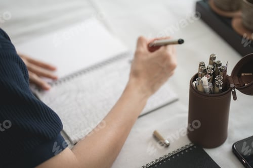 Preview: Close up and selective pens and pencils in brown pencil box with blurred hand writing on notebook.