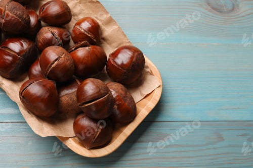 Preview: Fresh edible sweet chestnuts in serving plate on light blue wooden table, top view. Space for text