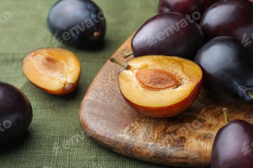 Preview: Many tasty ripe plums and wooden board on green fabric, closeup