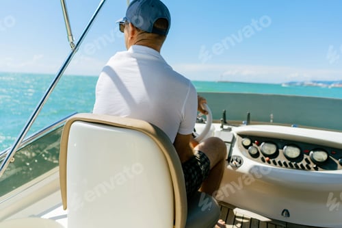 Preview: Bach view of middle-aged man driving luxury motor yacht. Captain at the helm of motor boat.