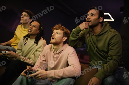 Preview: KYIV, UKRAINE - FEBRUARY 13, 2023: Focused indian man sitting near multiethnic friends playing video