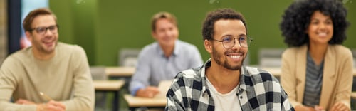 Preview: Young cheerful mixed race male office worker sitting listening to coach during seminar or training