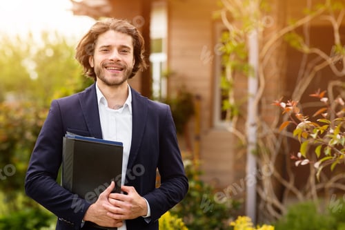 Preview: Portrait of happy real estate agent with documents posing near house outdoors