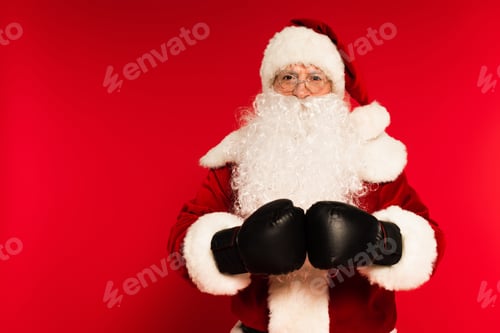 Preview: Bearded santa claus in boxing gloves looking at camera on red background