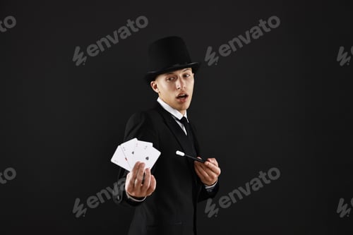 Vorschau: Illusionist, der Zauberstab auf Spielkarten vor schwarzem Hintergrund zeigt