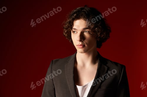 Preview: Curly haired young man showcases black stylish attire against bold backdrop