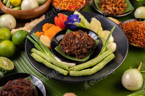 Preview: Chili paste is served on banana leaves on a plate with long beans, lime, chili, and eggplant.
