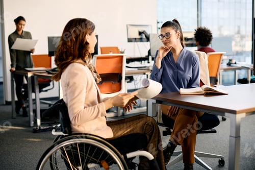 Preview: Happy businesswoman communicating with her colleague in wheelchair while working in the office.