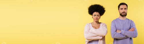 Preview: frustrated interracial couple looking at camera while standing with crossed arms isolated on yellow,