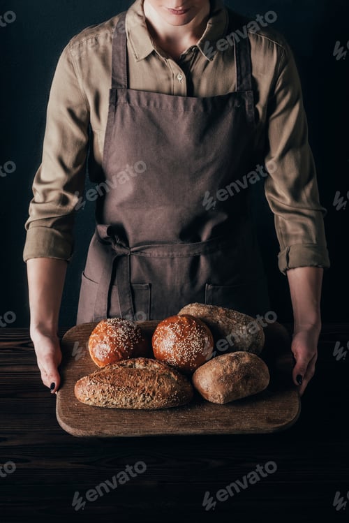 Preview: partial view of woman holding loafs of bread on wooden cutting board isolated on black