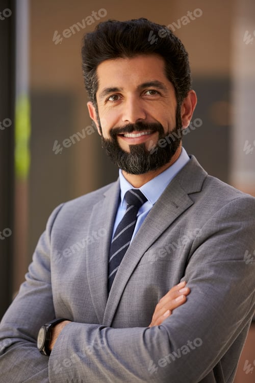 Preview: Smiling Hispanic businessman, arms crossed, close up vertical
