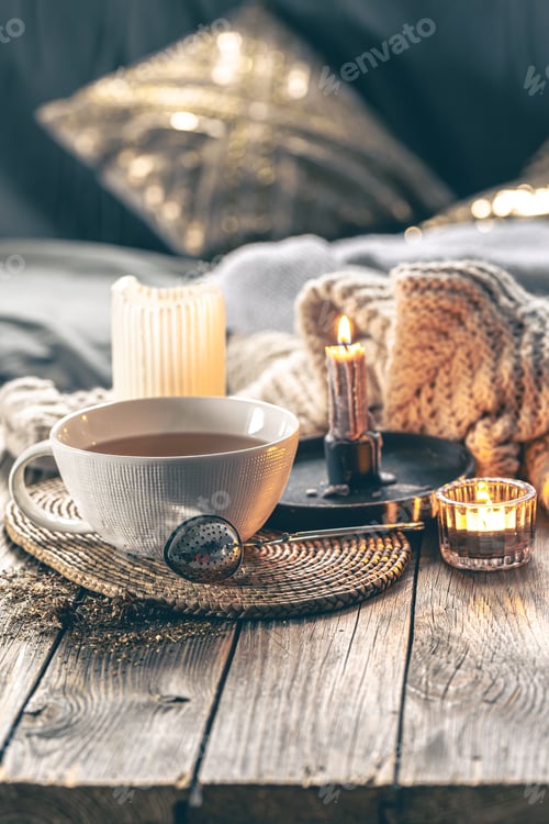 Preview: Cozy home composition with a cup of tea, candles and a knitted element.