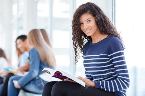 Preview: Portrait Of A Happy Woman Holding Book And Looking At Camera In University Hall