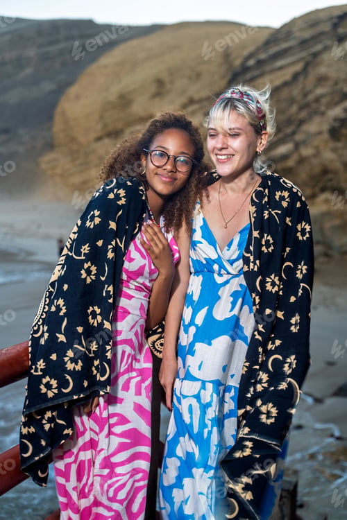 Preview: Two smiling young women leaving beach at sunset wrapped in towels