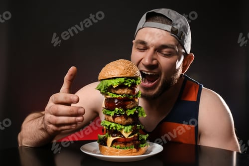 Preview: Young hungry man eating huge burger on black background