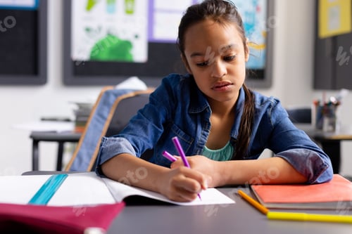 Preview: Child girl writing with purple pen in notebook at elementary classroom desk with binder, copy space