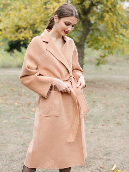 Preview: Young stylish woman in beige jacket having fun in the park