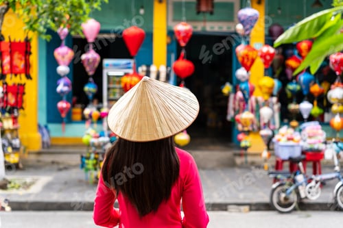 Preview: Young female tourist in Vietnamese traditional dress looking at a souvenir shop in Hoi An