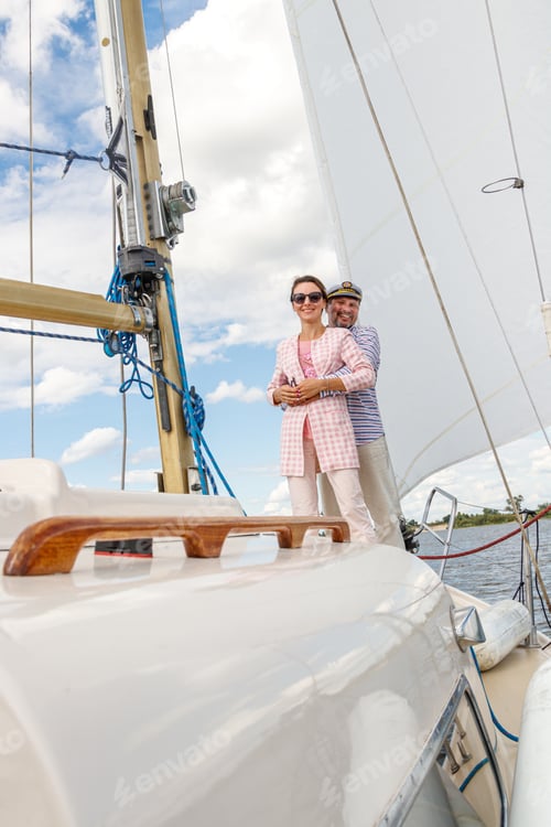 Preview: sailor man in a cap with a girl on a boat under sail against the sky and water
