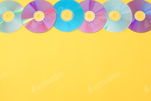 Preview: Colorful cds forming a row on a yellow background with copy space