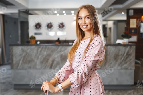 Preview: Young attractive woman with packed suitcase standing in hotel lobby