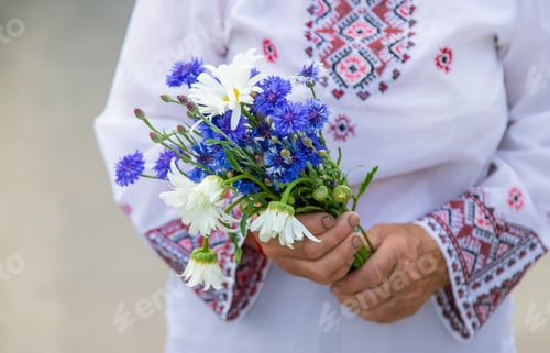 Preview: An old Ukrainian woman in an embroidered shirt with a bouquet of flowers. Selective focus.