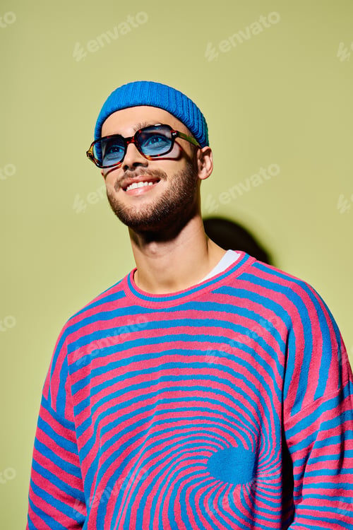 Preview: Young man flaunts vibrant fashion sense with stylish sunglasses in studio setting