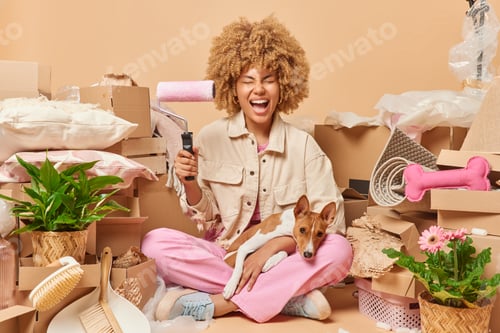 Preview: Housing repair and moving in concept. Positive curly woman holds paintr roller going to redecorate w