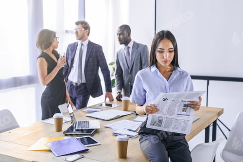 Preview: selective focus of asian businesswoman reading newspaper and colleagues having conversation behind