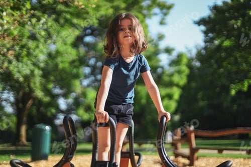 Preview: Caucasian beautiful little girl stands on a spinning swing in the park at the playground