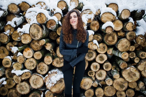 Preview: Elegance curly girl in leather jacket at snowy forest park at winter against stumps.